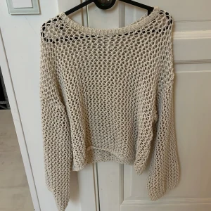 Beige stickad tröja från Monki - Säljer en beige stickad tröja från Monki i storlek L. Tröjan har ett grovmaskigt nätmönster och är långärmad med avslappnad passform. Perfekt att slänga över ett linne eller bikini för en chill look.