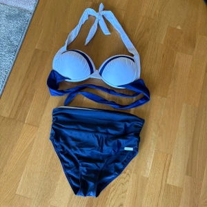 Blåvit bikini med hög midja - Snygg bikini från Panache i marinblått och vitt. Överdelen har vadderade kupor och knytband i nacken och ryggen. Underdelen är högmidjad med en vit kant upptill. Perfekt för strandhäng och pooldagar.