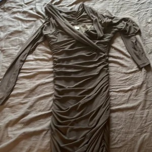 Svart omlottklänning från SHEIN - Snygg svart  kortklänning från SHEIN med omlott-detalj och långa ärmar. Klänningen har rynkade partier längs hela kroppen för en smickrande passform. Tillverkad i mjukt och stretchigt syntetmaterial, perfekt för dig som gillar trendiga och bekväma plagg.