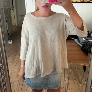 Guld glittrig topp med trekvartsärm - Säljer en guld glittrig topp med trekvartsärm och lös passform. Toppen har rund halsringning och ett lätt skimrande material som ger en snygg touch till outfiten. Perfekt att styla med jeans eller kjol för en trendig look.