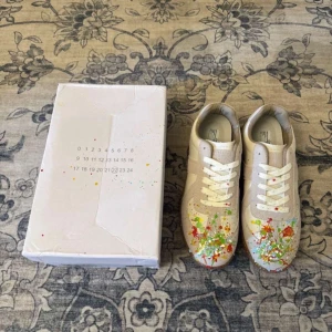 Maison Margiela gats  - Unika sneakers från Maison Margiela i beige och vitt skinn och mocka, med coola färgstänk i rött, grönt, gult och blått över tån. Klassisk gummisula och snörning. Perfekta för dig som vill sticka ut med en kreativ vibe.