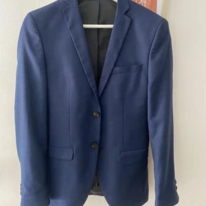 Kostym sett från jack and Jones - Säljes en mörkblå kostym från Jack & Jones. Inköpt i maj och använd vid ett tillfälle.  Kavajen har storlek 42. Byxorna storlek 44.  Kommer en fluga och en vit skjorta med på köpet.  Nypris 2100:- Mitt pris 1.500 Kvitto finns.  