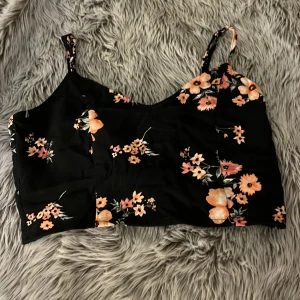 Svart blommig linnetopp från Divided!! - Säljer en svart croppad linnetopp från Divided med orange och rosa blommor!!💐Toppen har smala axelband, v-ringning och knyt i ryggen. Perfekt för varma dagar!!☀️kKnytningen i ryggen gör den extra detaljerad och söt!!☺️ Går både att klä upp och ner! Hör av er om ni har frågor eller vill ha fler bilder eller mått!!🥰