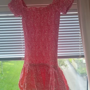 Rosa klänning från H&M XS - Supersöt rosa kortklänning från H&M i storlek XS. Klänningen har vita mönster, offshoulder-modell och korta puffärmar. Volang nertill ger en extra feminin touch. Perfekt för varma dagar och somriga vibes!