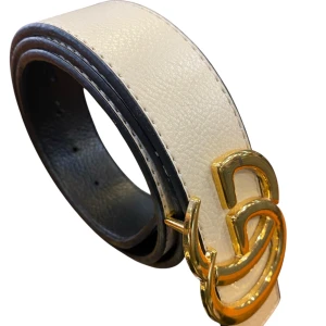  vitt skärp med guldspänne - Snyggt vitt bälte i äkta skinn med ikoniskt dubbelt spänne i guld. Bältet har en stilren och klassisk design med svarta kanter och struktur i lädret. Perfekt accessoar för att lyfta din outfit.