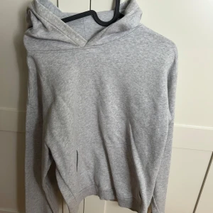 Ljusgrå hoodie med huva - En stilren ljusgrå hoodie med huva och långa ärmar. Tröjan har en klassisk passform och är tillverkad i mjukt bomullsmaterial. Perfekt för chill dagar eller när du vill ha en enkel och clean look.
