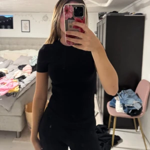 Svart tight ribbad T-shirt  - En svart, tight ribbad  t-shirt med korta ärmar. Enkel och stilren modell som sitter figurnära och är gjord i mjukt bomullsmaterial. Perfekt till jeans eller kjol för en clean look.