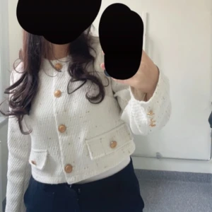 Vit kofta med guldknappar - Snygg vit kofta i kort modell med dekorativa guldknappar framtill och på fickorna. Koftan har två fickor och är tillverkad i ett strukturerat tyg som ger en exklusiv känsla. Perfekt för dig som gillar stilrena och trendiga plagg.