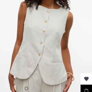 Ljus skräddarsydd väst  - Snygg ljusbeige skräddarsydd väst med knappar framtill och två fickor. Västen har en stilren, rak passform och justerbart bälte i ryggen för extra passform. Perfekt att styla med matchande byxor för en clean look. Helt ny, utan prislapp.