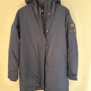 Blå parkas från Peak Performance M - Säljer en stilren blå parkas från Peak Performance med huva och stora fickor framtill. Nästan aldrig använd nypris ca 3000 kr