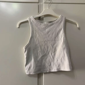 Vit ribbad croppad linnetopp - Säljer en vit croppad linnetopp med ribbad struktur. Toppen är ärmlös och har en klassisk rund halsringning. Perfekt för att styla med jeans eller kjol för en clean och fräsch look.