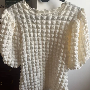 Vit blus med puffärmar - Unik vit blus med coolt quiltat rutmönster och stora puffärmar. Blusen har en tightare passform och är tillverkad i ett mjukt bomullsmaterial. Perfekt för dig som gillar statement-plagg med textur och volym. Rund halsringning och snygga detaljer längs kanterna.