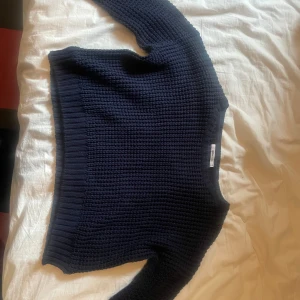 Mörkblå stickad tröja från Gina Tricot - Mysig mörkblå stickad tröja från Gina Tricot med grov struktur och rund hals. Tröjan har långa ärmar och ribbade muddar vid ärmslut och nederkant. Perfekt för lager-på-lager och chill dagar.