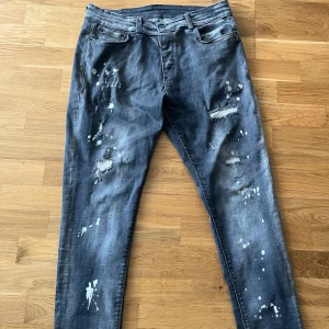 Dsquared2 blå distressed jeans - Snygga blå jeans från Dsquared2 med slitningar, färgstänk och lagade detaljer för en rå streetlook. Klassisk femficksmodell med normal passform och medelblå tvätt. Jeansens material är bomull och de har Dsquared2-logga vid gylfen samt patch bak.
