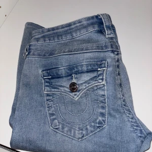 True Religion Joey ljusblå flare jeans - Säljer ett par ljusblå True Religion Joey jeans med låg midja och flare-ben. Perfekta för dig som gillar retrovibbar och vill sticka ut med coola detaljer. Uppsydda något men passar för dig som är 165, bra skick. 