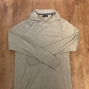 Beige stickad half zip från Jack & Jones - Snygg beige stickad tröja från Jack & Jones i storlek M. Tröjan har en hög krage med half zip-dragkedja och långa ärmar. Perfekt för dig som gillar stilrena och enkla plagg med en chill vibe. Passar bra till jeans eller chinos.