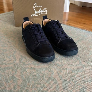 Mörkblå sneakers från Christian Louboutin - Snygga svarta sneakers från Christian Louboutin i mocka med klassisk röd sula. Skorna har rund tå, svarta snören och diskret logga på hälen. Insidan är beige och de har en stilren, använda ett fåtal gånger och i toppskick, pris kan diskuteras! Hör av dig vid minsta fråga eller fundering!