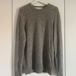 Grå stickad tröja från A Day's March - En klassisk grå stickad tröja från A Day's March i storlek medium. Tröjan har rund halsringning, ribbade muddar och är långärmad. Perfekt för lager-på-lager och enkel att matcha med jeans eller chinos.