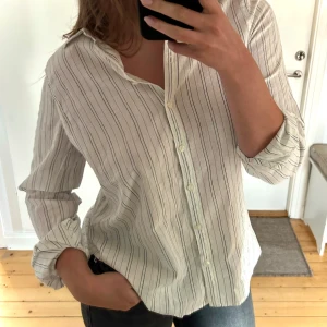 Randig skjorta - Lindex - Helt ny klassisk vit skjorta med tunna svarta ränder från Holly & White (Lindex). Rak och något lös passform i ett lätt och bekvämt material som passar perfekt både till vardags och på jobbet.