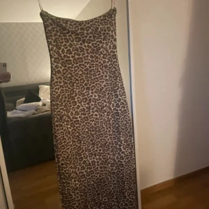 Leopardmönstrad långklänning - Säljer en snygg långklänning med leopardmönster och tunna axelband. Klänningen har en rak passform och är perfekt för dig som vill sticka ut. Materialet känns mjukt och följsamt mot kroppen. Perfekt att styla med boots eller klackar.