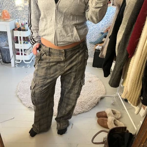 Gröna rutiga cargopants med fickor - Säljer ett par gröna cargopants med rutigt mönster och flera stora fickor på sidorna. Byxorna har låg midja och en loose passform, perfekta för en chill och avslappnad stil. Materialet känns slitstarkt och de har coola detaljer som knappar och dragkedjor på fickorna.