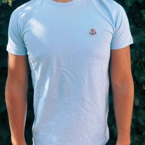 Ljusblå t-shirt från Moncler - Fräsch ljusblå t-shirt från Moncler med klassisk rund hals och korta ärmar. T-shirten har en liten Moncler-logga på bröstet och är gjord i mjuk bomull som känns skön mot huden. Perfekt för dig som gillar stilrena och enkla plagg.                                                                                                                                                                              Nypris: 2000kr GORILLAPRIZE:1120kr            Skick:10/10 oöppnad         KVITTO MEDKOMMER     
