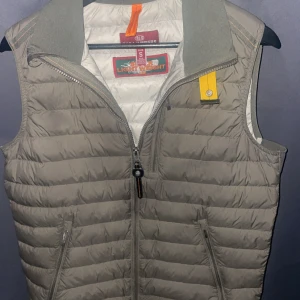 Grön dunväst från Parajumpers - Säljer en grön dunväst från Parajumpers i modellen Super Lightweight. Västen har quiltad design, dragkedja framtill och två fickor med dragkedja. Snygg orange detalj vid kragen och klassisk Parajumpers-logga på insidan. Perfekt för lager-på-lager-stil. Pris kan diskuteras 