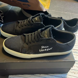 Svarta Saint Laurent sneakers - Ny pris ca 16 tusen. Svarta sneakers från Saint Laurent med vit logga broderad på sidan. Skorna har en klassisk låg profil, snörning och vit platt sula. Ovandelen är i canvas och detaljer i skinn, vilket ger en stilren och trendig look. Kan gå ner i pris vid snabb affär. Fraktar samma dag och skicket är i 6/10