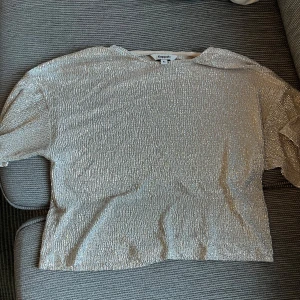 Glittrig silver topp från Kappahl - Säljer en glittrig silver topp från Kappahl i storlek XS. Toppen har korta ärmar och är täckt av skimrande paljetter som ger en riktigt festlig look. Perfekt för dig som vill sticka ut och glänsa lite extra.
