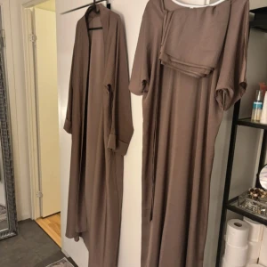 Brun/mocha brun Dubai abaya set | 4 delar - Helt ny, endast testad för bild. Tyvärr kommer jag ej att gå ner i pris. Fast pris! Inköpt i Dubai för 1450kr  Str 56 Kommer i 4 delar- Abaya, underabaya , matchande hijab +bälte  -lightweight, thin and silky ✨ -materialet är det skönaste, väldigt tunt och svalt ( inte genomskinligt ) Material: vet ej, kan ej svara på det  -sista bild är för jag täckte håret med vit penna, inget fel på den!☺️