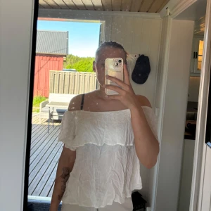 Vit offshoulder blus - Säljer en vit offshoulder blus med volangdetalj. Blusen är luftig och har en avslappnad passform, perfekt för varma dagar. Tillverkad i ett lätt material som ger en somrig känsla.