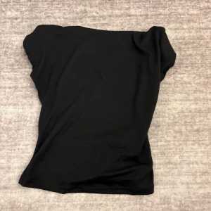 Svart topp med öppen rygg - En enkel svart topp i mjukt material. Toppen har en rak och något bredare halsringning och är figurnära i modellen. Perfekt att matcha med jeans eller kjol för en stilren look.