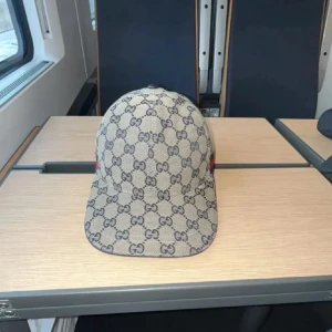 Beige keps från Gucci med GG-mönster - Säljer en beige keps från Gucci med klassiskt GG-mönster över hela kepsen. Kepsen har justerbart spänne bak och en röd-blå rand på sidan. Materialet är bomull och syntet, och passformen är normal.
