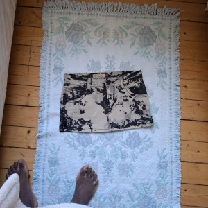 Svartvit batikmönstrad jeanskjol från Fallback - Cool kort jeanskjol från Fallback med svartvit batikmönster. Klassisk femficksmodell med knapp och dragkedja framtill. Perfekt för dig som vill sticka ut med en unik stil.