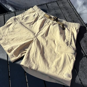 Beige shorts från The North Face - Snygga beige shorts från The North Face med elastisk midja och justerbart bälte. Shortsen har flera fickor och är perfekta för varma dagar. Lätt och bekvämt material som passar till många tillfällen.