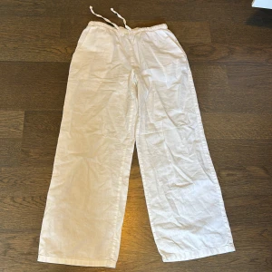 Vita linnebyxor från Gina Tricot - Säljer ett par vita linnebyxor från Gina Tricot med dragsko i midjan. Byxorna har raka, vida ben och är tillverkade i ett tunt och luftigt linnematerial. Perfekta för varma dagar och enkel att matcha med olika toppar.