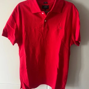 Röd pikétröja från Boomerang - Säljer en klassisk röd pikétröja från Boomerang i modellen Joe Classic Fit. Tröjan har korta ärmar, krage och knäppning med två knappar framtill. Perfekt för en stilren och avslappnad look. Piken är även endast använd en gång.