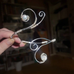 HANDGJORT Silvrigt armband, äkta pärlor och snirklig design - Unikt handgjort armband i silverfärgad metall med två vita pärlor. Armbandet har en snirklig, elegant form som slingrar sig runt armen och ger en bohemisk känsla. Perfekt för dig som vill sticka ut med ett personligt smycke. Äkta sötvatten pärlor, silver rostar inte