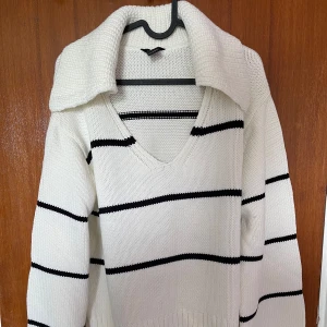 Vit stickad tröja med svarta ränder från Lindex - Säljer en vit stickad tröja från Lindex med svarta horisontella ränder. Tröjan har v-ringning, lång ärm och en bred krage. Perfekt för en stilren och avslappnad look. 