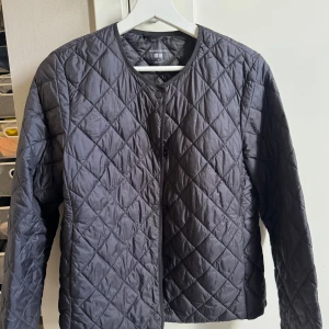 Svart quiltad jacka från Uniqlo - Säljer en svart quiltad jacka från Uniqlo i storlek S. Jackan är lätt vadderad och har rund halsringning samt knäppning framtill. Perfekt som ett extra lager under kyliga dagar.