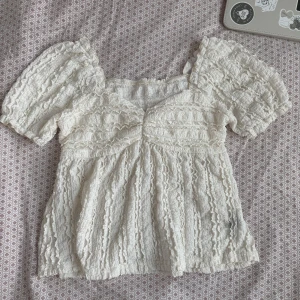 Vit blus med puffärmar - Säljer en söt vit blus med spets och puffiga korta ärmar. Blusen har en fyrkantig ringning och fina volangdetaljer över hela tyget. Perfekt för dig som gillar romantisk stil!