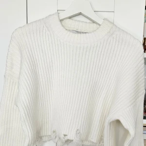 Vit croppad stickad tröja - Säljer en vit croppad stickad tröja med ribbad struktur och råa kanter nertill. Tröjan har långa ärmar och en rund halsringning. Perfekt för dig som gillar en trendig och avslappnad stil.