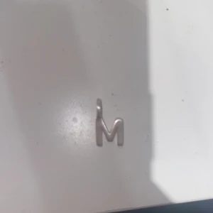 Silverfärgad bokstavsberlock M - Säljer en stilren berlock i form av bokstaven M i silverfärg. Perfekt att hänga på ett halsband eller armband för en personlig touch. Enkel och modern design som passar till många olika stilar. Knappt använd!