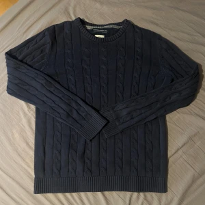 Mörkblå kabelstickad tröja från Jack & Jones - Säljer en mörkblå kabelstickad tröja från Jack & Jones. Tröjan har rund halsringning och långa ärmar. Klassisk och stilren design med ribbade muddar vid ärmslut och nederkant. Perfekt för kyligare dagar. Den är i storlek s men passar öven m. Passar mig (184 cm)