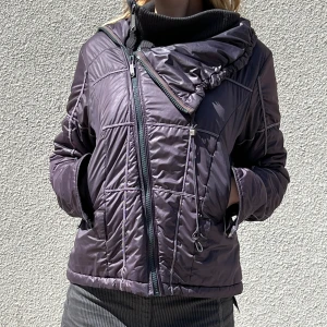 Diesel pufferjacka med sned dragkedja - Säljer min mörkgrå/lila pufferjacka från Diesel med sned dragkedja och polo detalj. Jackan har långa ärmar, två fickor framtill och quiltad design.   Påminner starkt om Rick Owens och Drkshdw. Säljer billigare då det inte är säsong men jag vill rensa min garderob. Storlek 36. S. Bra för vår och höst, om med varma lager så fungerar den på vintern också.