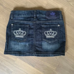 Jeanskjol Victoria Beckham Rock & Republic vintage - Säljer en vintage mörkblå jeanskjol från Victoria Beckham Rock & Republic. Kjolen har två bakfickor med broderade kronor och små nitar som detalj. Klassisk jeanslook med bälteshällor och markerad söm. Strl M men är S/M. Se mina övriga annonser för mer äkta Y2K.