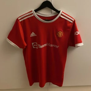 Röd Manchester United fotbollströja 21-22 - Säljer en röd Manchester United fotbollströja från Adidas med korta ärmar. På baksidan finns namnet 'Ronaldo' och nummer 7. Priset kan diskuteras 