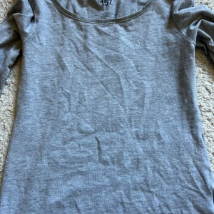 Grå långärmad topp från 157 - En basic grå långärmad topp från 157 med rund halsringning. Tillverkad i mjuk bomull, perfekt att styla lager på lager eller bära som den är. Enkel och stilren design utan mönster eller detaljer.