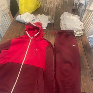 Vinröda mjukisbyxor och Hoodie från BOSS - Säljer ett par vinröda mjukisbyxor från BOSS med dragsko i midjan och diskret logga på benet. Byxorna har en avslappnad passform och är perfekta för chill dagar. Matchar med hoodie i samma färg.