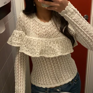 Vit blus med volang - Säljer en superfin vit blus i spets med volangdetalj över bröstet. Blusen är figurnära och har långa ärmar. Använd 2 gånger 